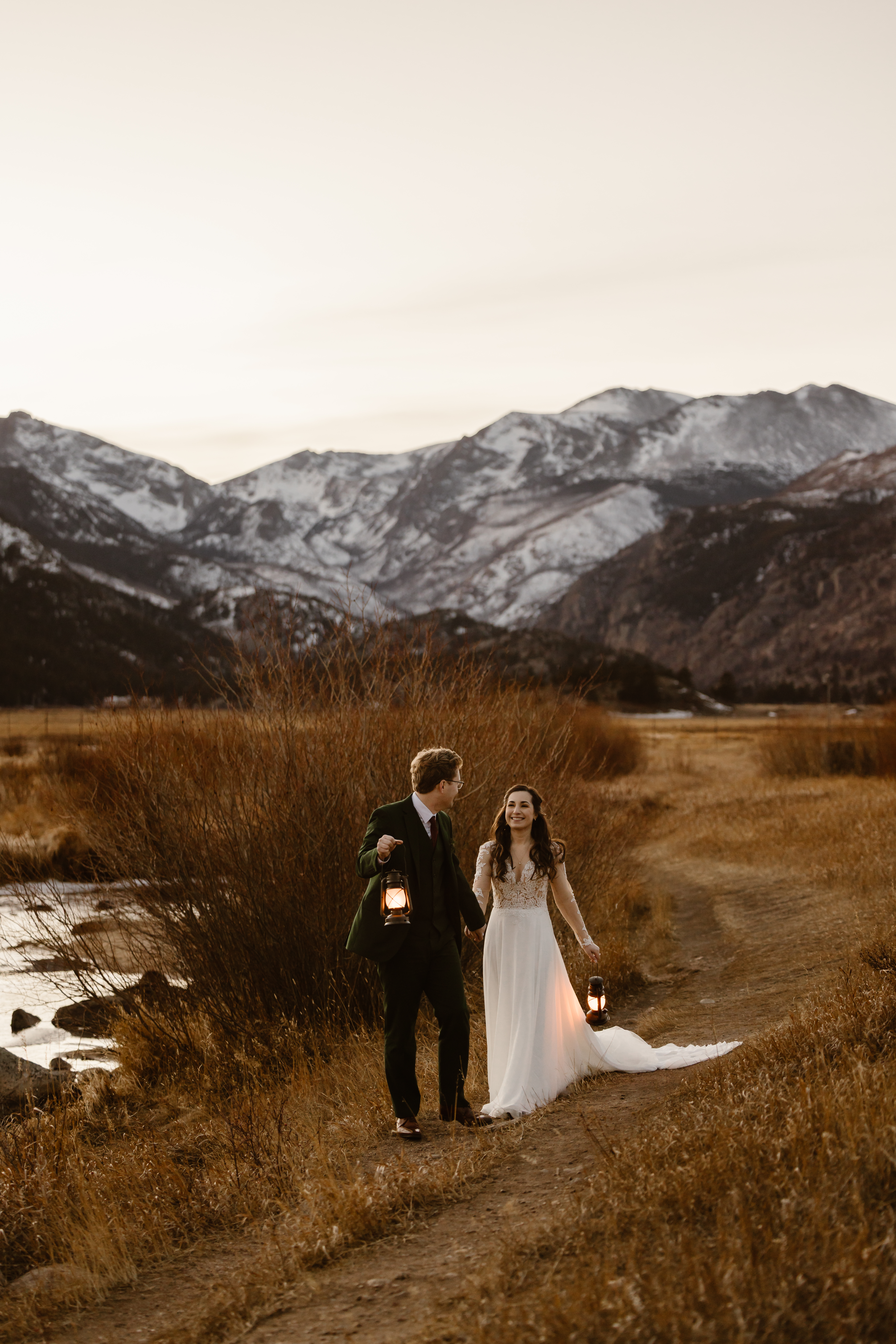 Bride and groom walking along a mountain trail at sunset during their December elopement in Rocky Mountain National Park holding lanterns.