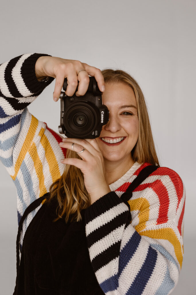Cassie Peterson smiling while holding a Canon camera, Colorado elopement photographer and planning guide.