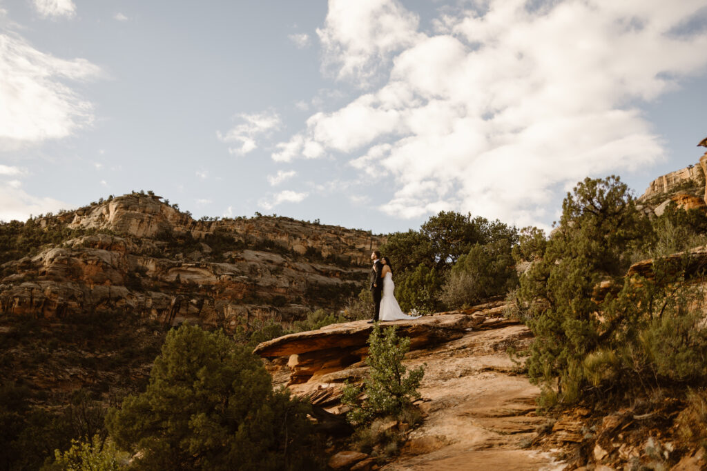 Bride and groom standing on a red rock ledge during an October elopement in Colorado with warm desert tones and soft clouds overhead.