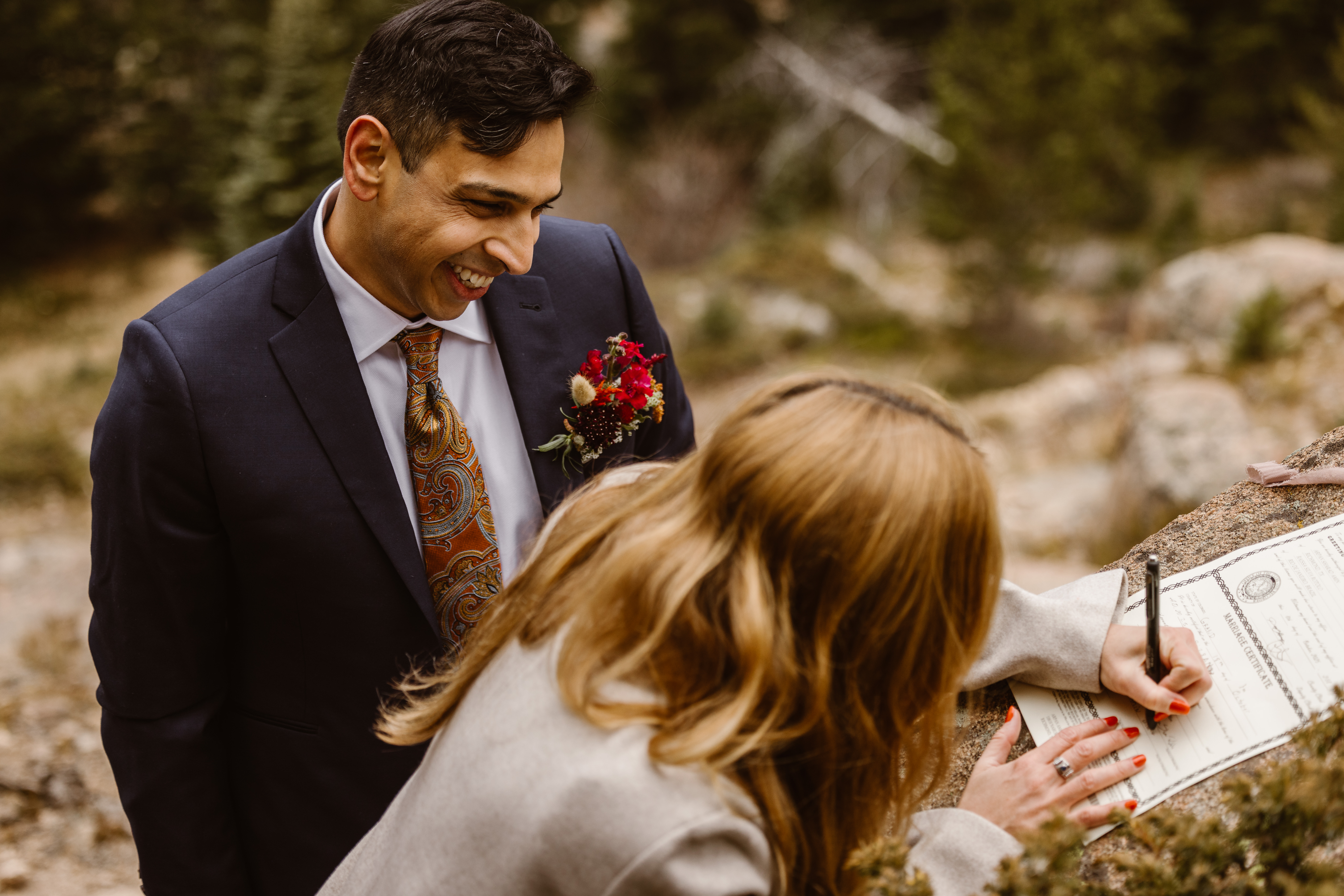 Bride signing their Colorado marriage license during a self-solemnization elopement ceremony while their partner smiles beside them outdoors.