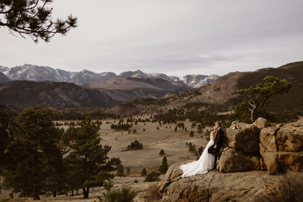 Couple together on a rocky overlook in Rocky Mountain National Park during their Colorado elopement, with mountain peaks stretching across the background.