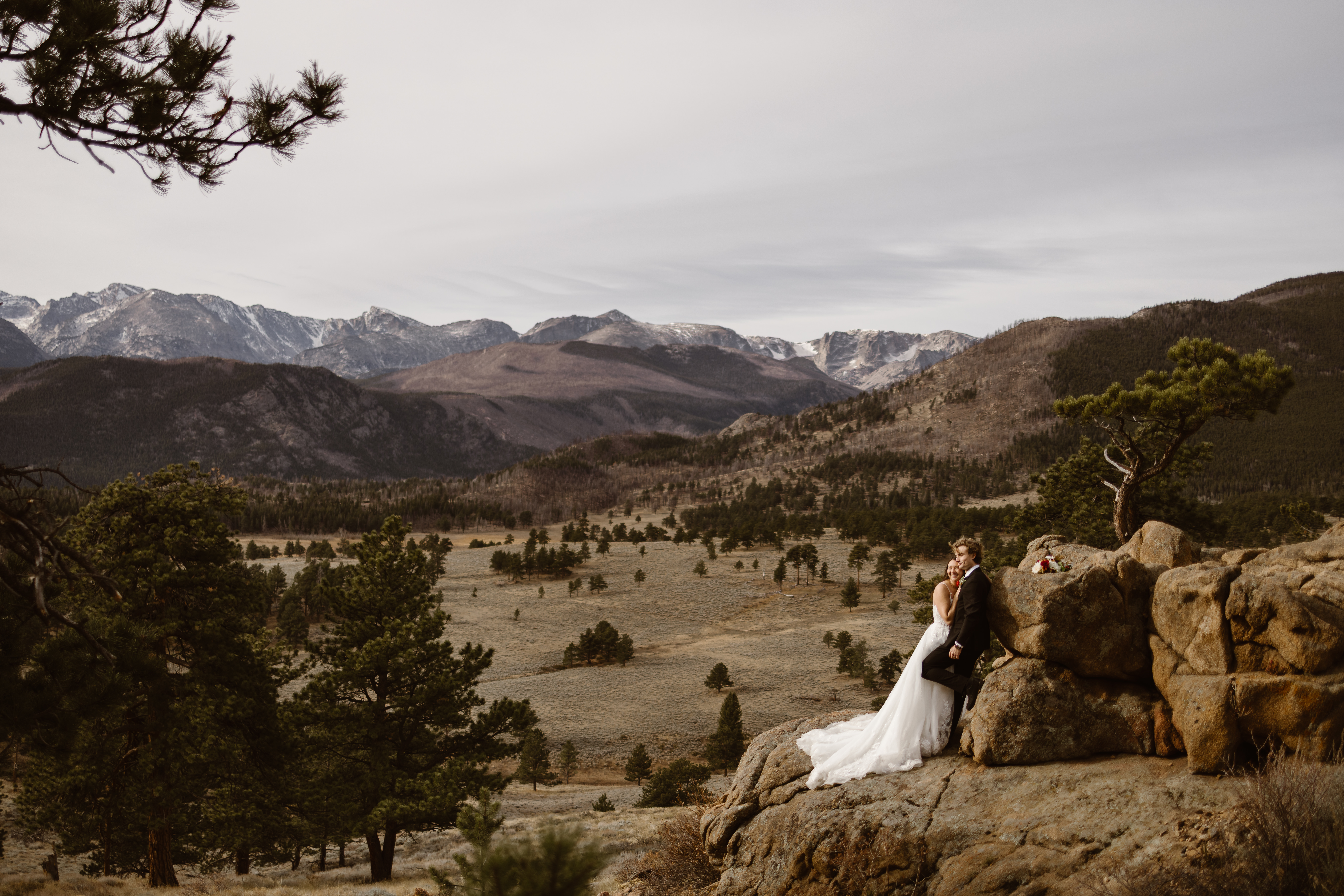 Couple together on a rocky overlook in Rocky Mountain National Park during their Colorado elopement, with mountain peaks stretching across the background.