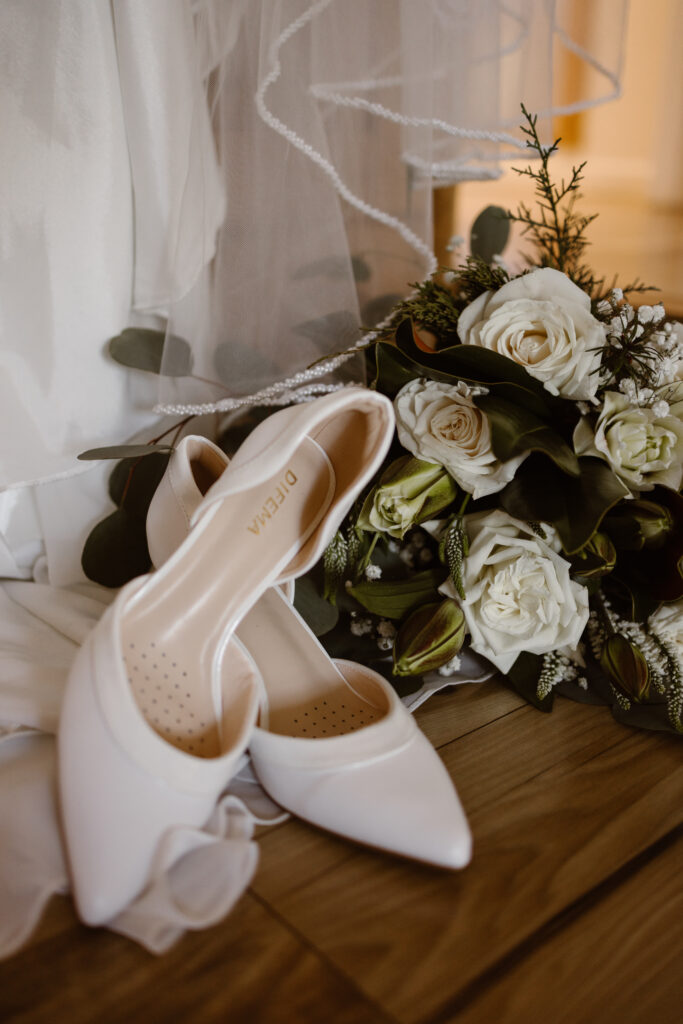 White bridal shoes placed beside a bouquet and veil during elopement getting ready details.