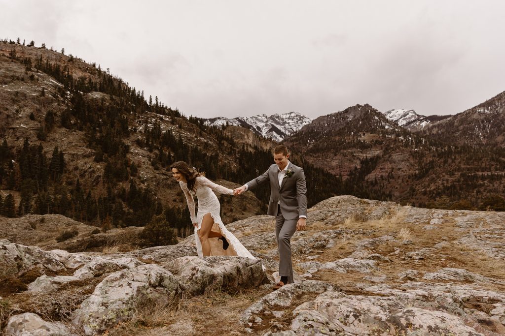 Bride and groom run hand in hand across rocky terrain during their elopement in Ouray, Colorado, surrounded by mountain views.