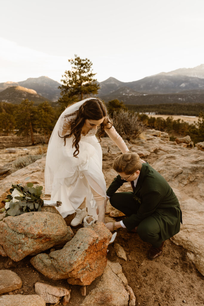 Groom helps bride step down rocky terrain during a winter elopement in Rocky Mountain National Park with mountains in the background.