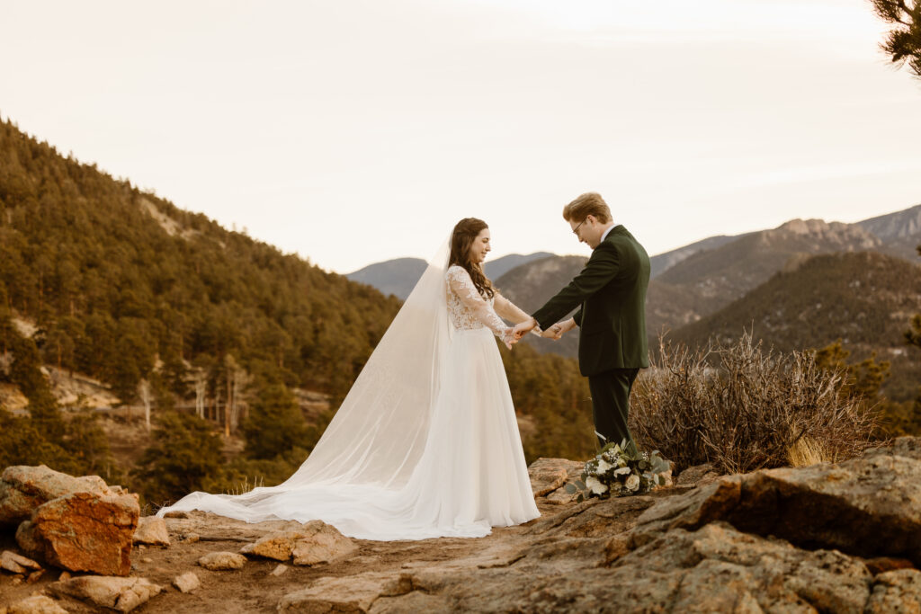Bride and groom hold hands while standing on a rocky overlook during a winter elopement in Rocky Mountain National Park.