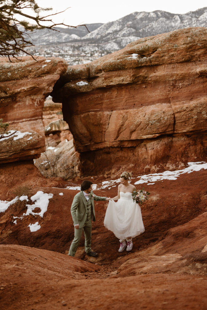 Bride and groom walk hand in hand through the red rock formations at Garden of the Gods during their winter elopement in Colorado.