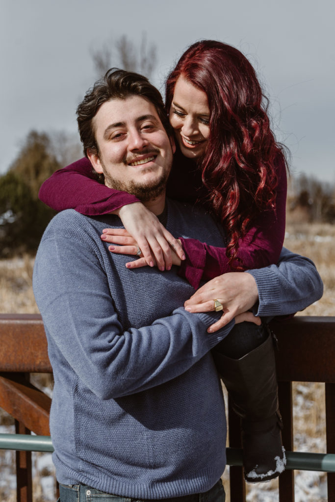 Woman behind her fiancé with her arms around him