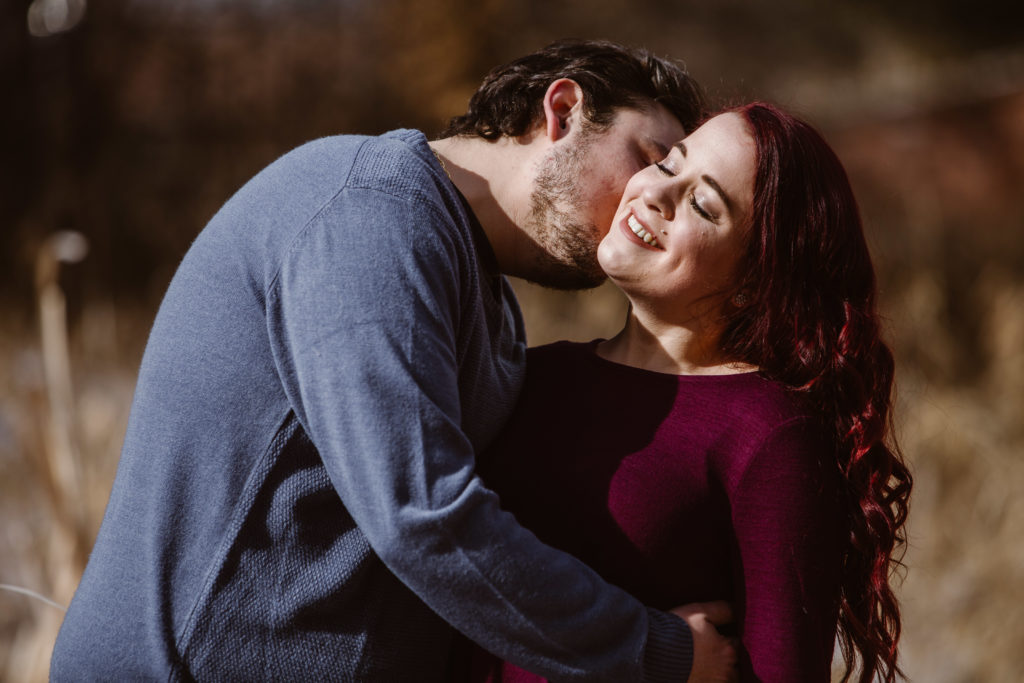 Man kissing his fiancé's neck, she is smiling with her eyes closed