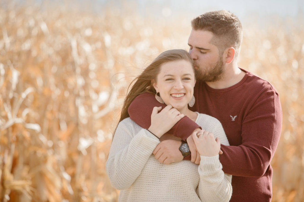 Man standing behind his fiancé kissing her temple