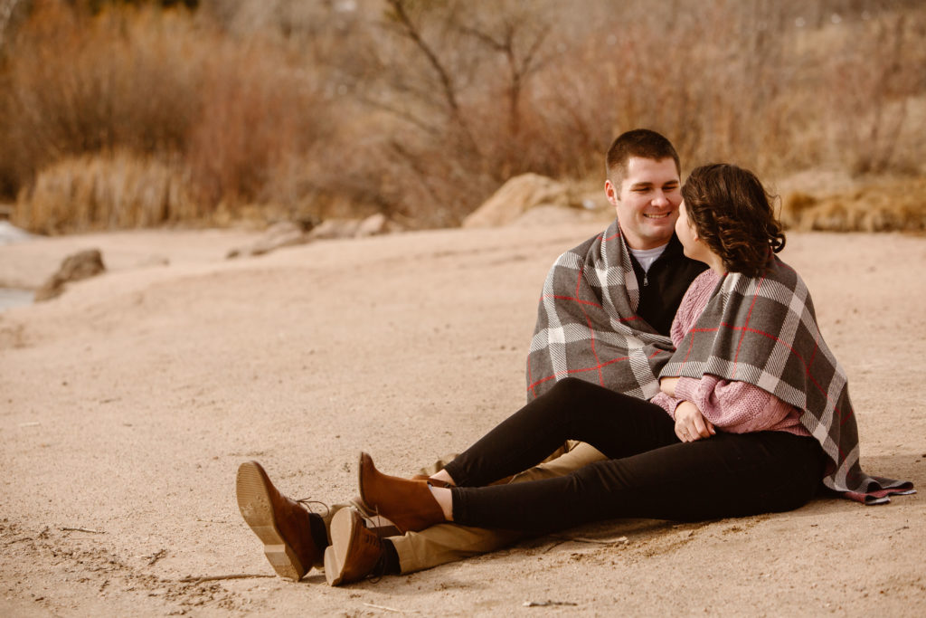 Couple wrapped in a blanket looking at each other on a sandy beach
