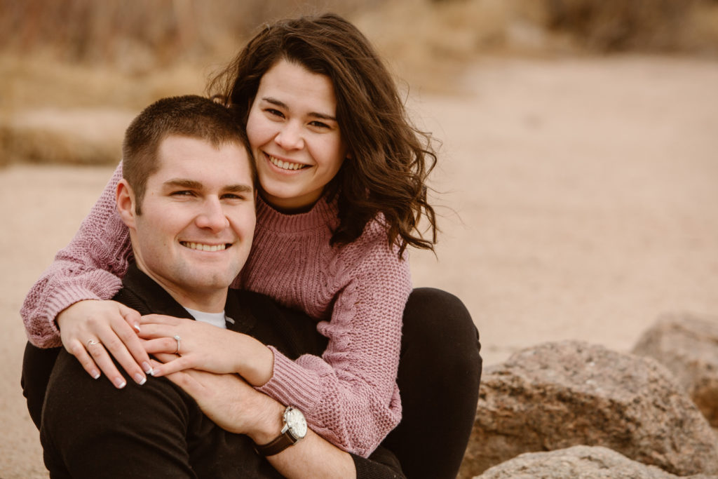 Woman behind her fiancé with her arms around him, both of them smiling