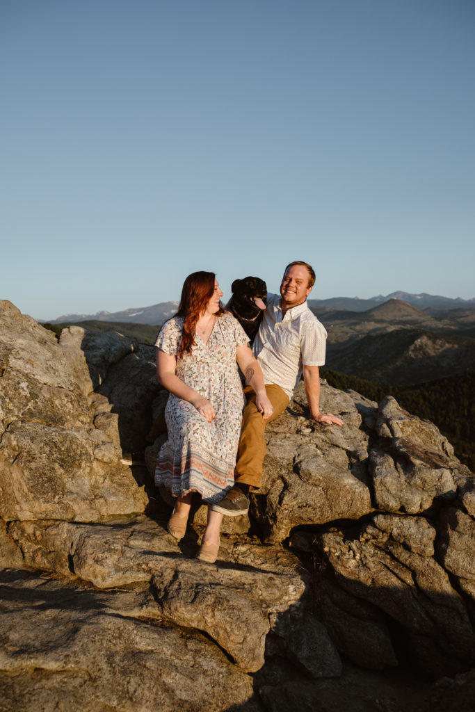 Couple sitting on a rock with their dog laughing