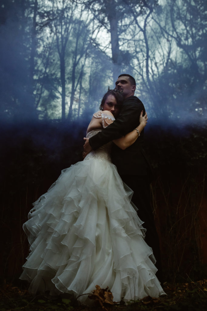 Bride and groom holding hands with colored smoke behind them.
