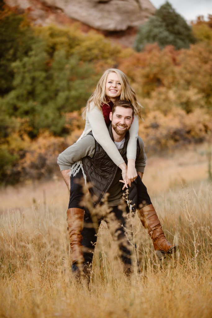 Couple with a woman on a mans back, arms wrapped around him and they are both smiling