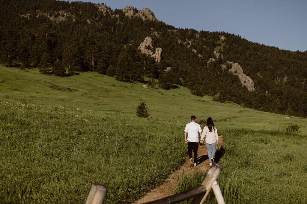 Engaged couple walking down a dirt path hand in hand