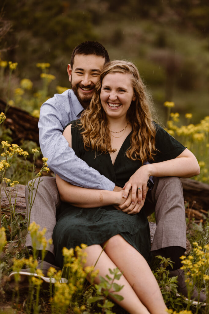 Man behind his fiancé with his arms wrapped around her. They are both smiling