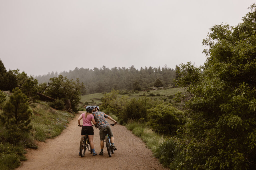 Engaged couple sharing a kiss while stopped on their mountain bikes on a dirt path