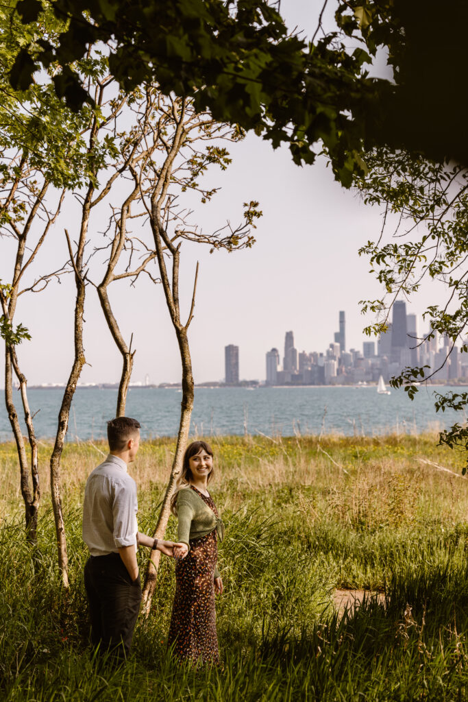 Woman leading her fiancé down a path with the Chicago skyline in the background