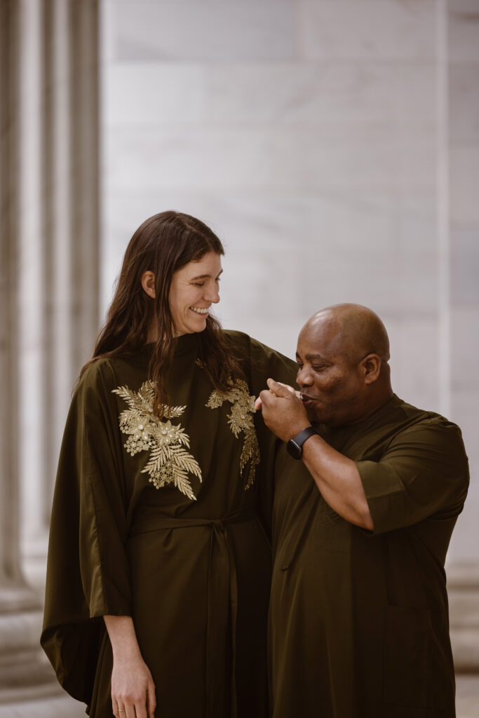 Couple in Nigerian outfits man kissing his fiancé's hand with her smiling