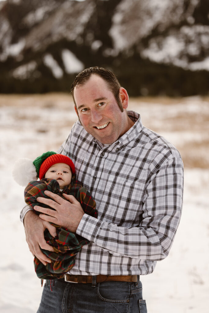 Father holding his newborn daughter with snowy Flatirons in the background