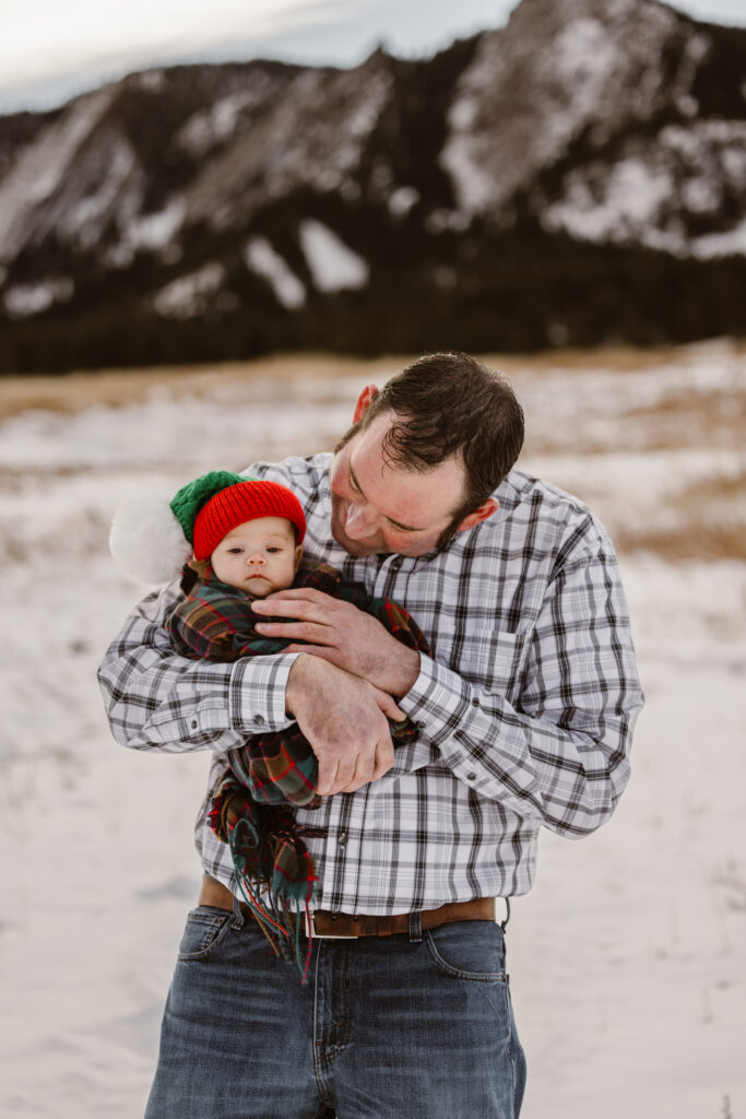 Father looking at his newborn daughter with snowy Flatirons in the background