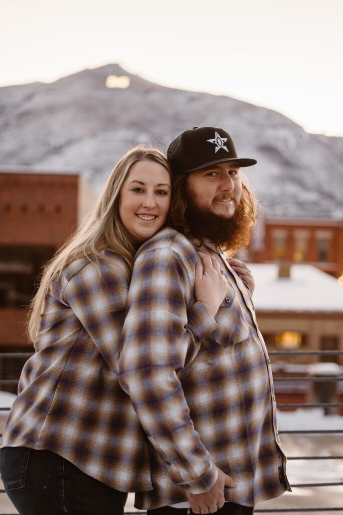 Woman with her arms wrapped under her boyfriend's arms with a snowy mountain in the background