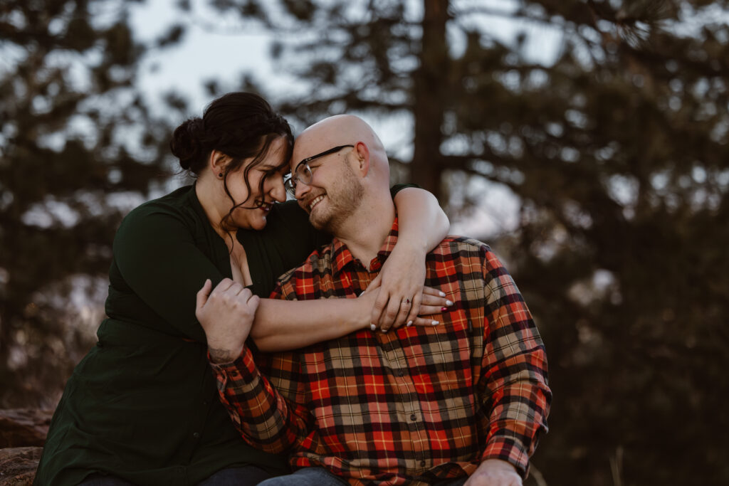 Couple sitting next to each other with her arms wrapped around his shoulders while touching foreheads