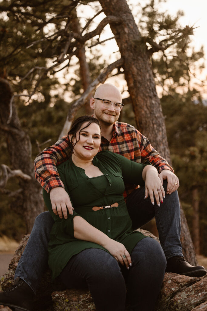 Couple sitting on a rock, with the woman in front if him, snuggled up