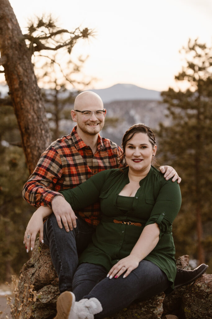 Couple sitting on a rock, with the woman in front if him, snuggled up