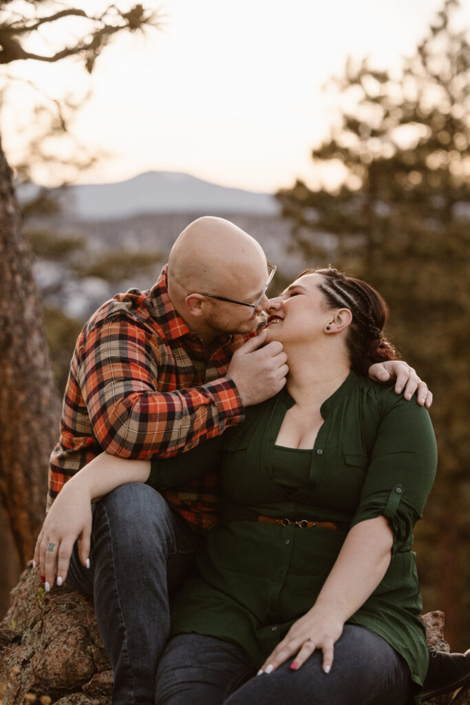 Couple sitting on a rock, with the woman in front if him, leaning in for a kiss