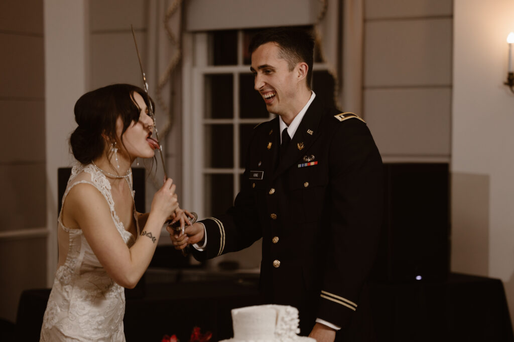 Bride and groom cutting their wedding cake with a sword, bride licking the frosting off a the sword