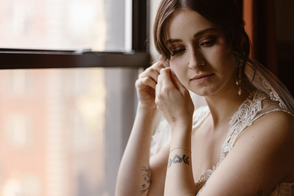 Bride putting earring in by window