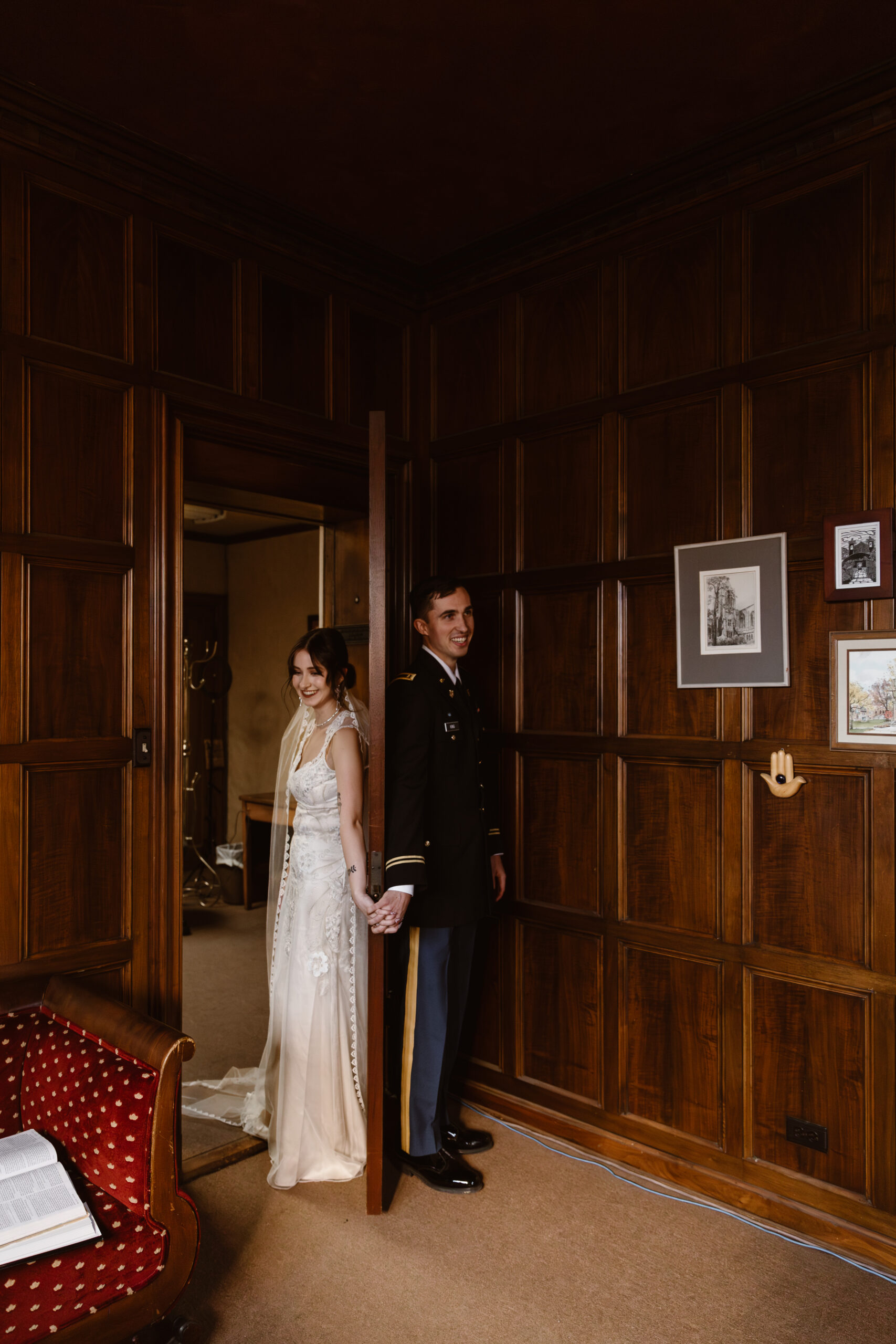 Bride and groom first touch. Their backs are against a door and they are holding hands without seeing each other