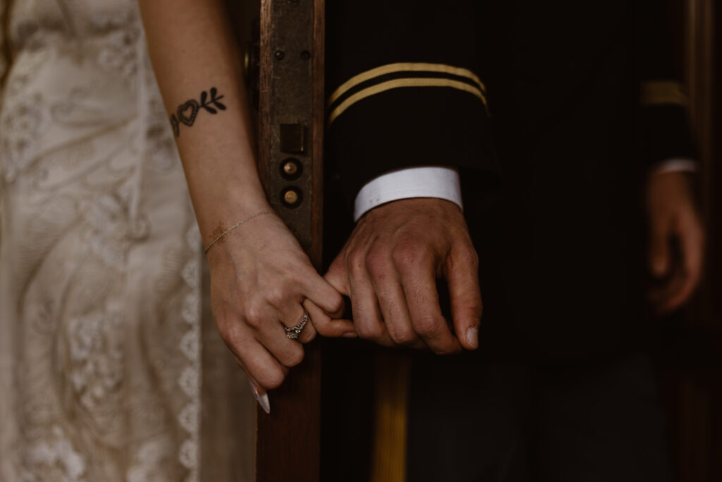 Bride and groom linking pinkies during first touch at their wedding. A door is between them with their backs to it