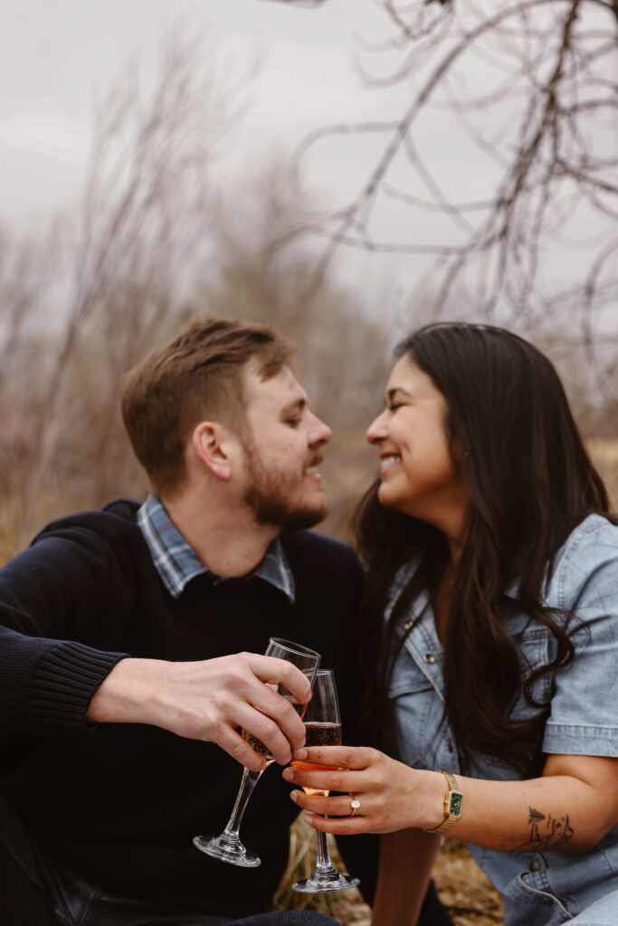 Engaged couple cheersing with champagne about to kiss on a blanket