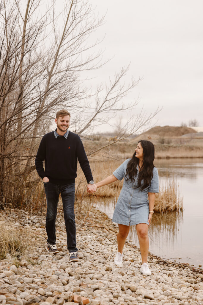 Couple walking hand in hand looking at each other smiling by a lake