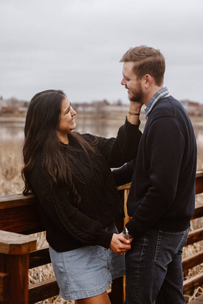 Couple facing each other holding hands, woman had her hand on his cheek, smiling