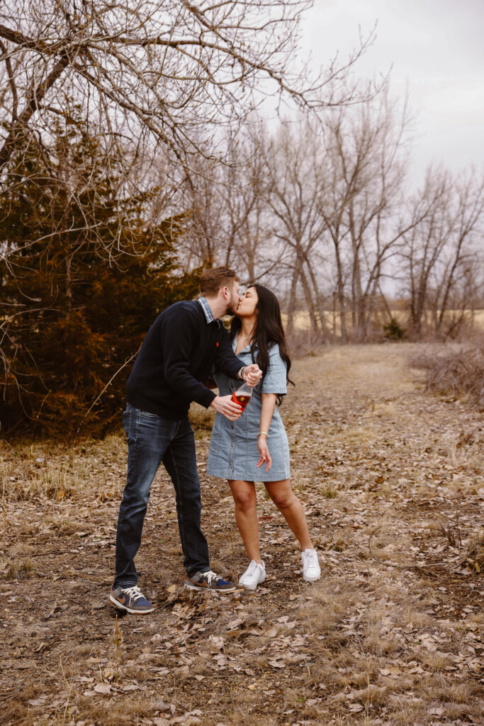 Man spraying bottle of champagne kissing his fiancé