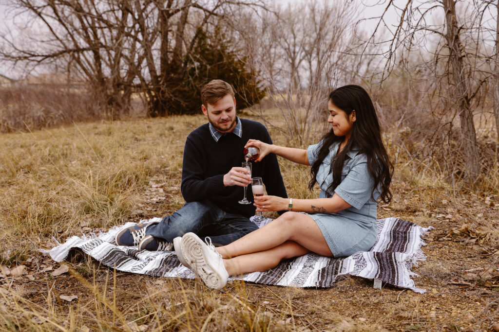 Woman pouring champagne into glasses with her fiancé on a blanket