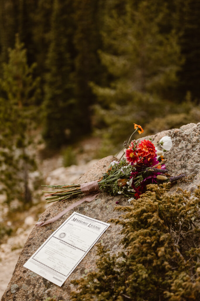 Signed Colorado marriage license and colorful wildflower bouquet resting on a rock during an intimate Winter Park elopement in the mountains.