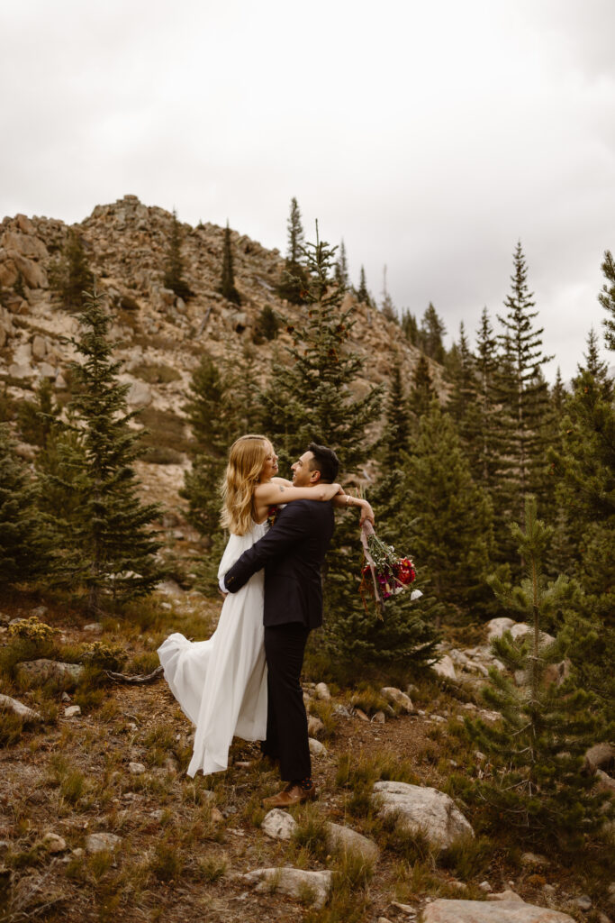 Just-married couple sharing a joyful lift and embrace during post-ceremony portraits in the forest near Winter Park, Colorado.