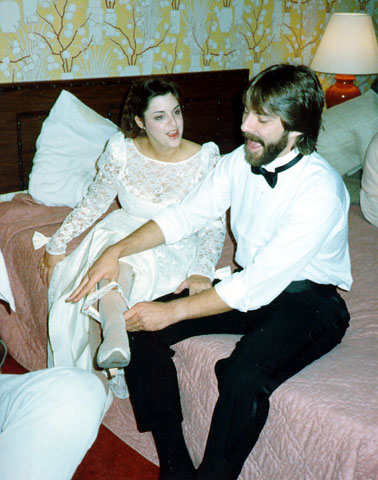Bride and groom laughing during a playful garter moment in their hotel room after their vintage Las Vegas elopement.
