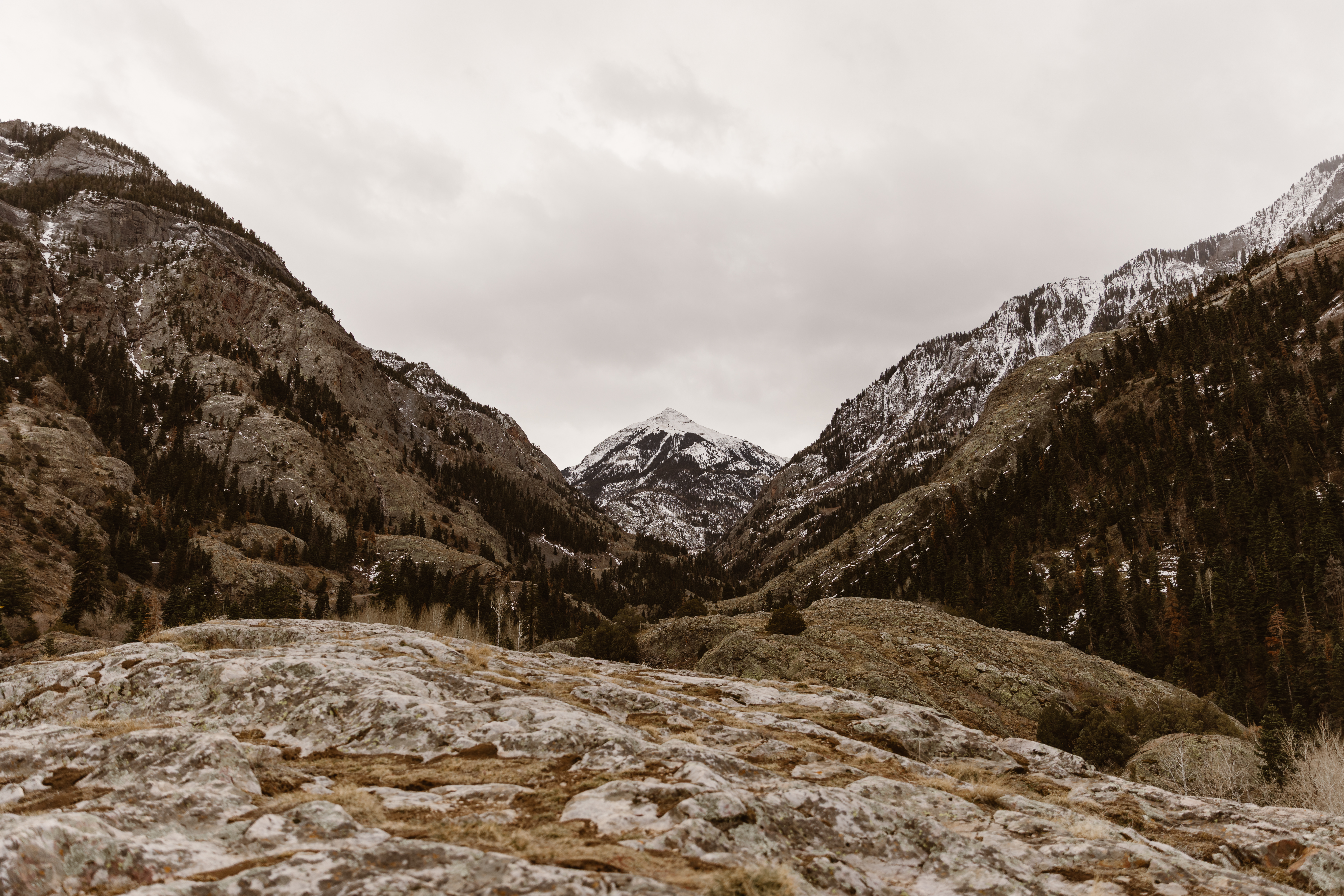 Wide view of a Colorado mountain valley with light snow on the ground and overcast skies settling between rugged peaks.