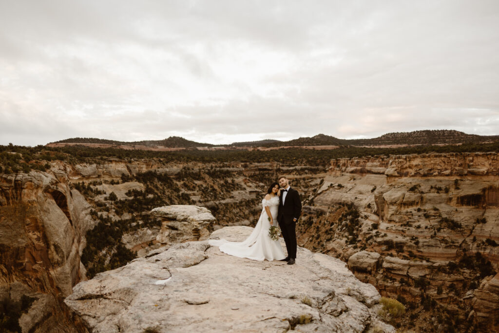 Bride and groom standing on a canyon overlook during their Colorado elopement with layered desert cliffs stretching into the distance.