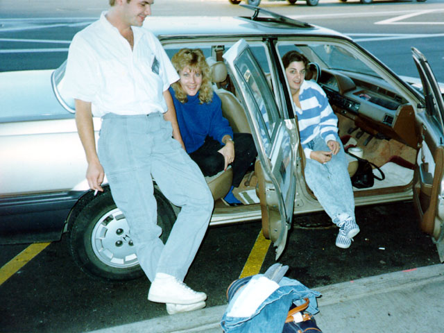 Newly married couple with a family member beside a car at the airport after their vintage Las Vegas elopement.